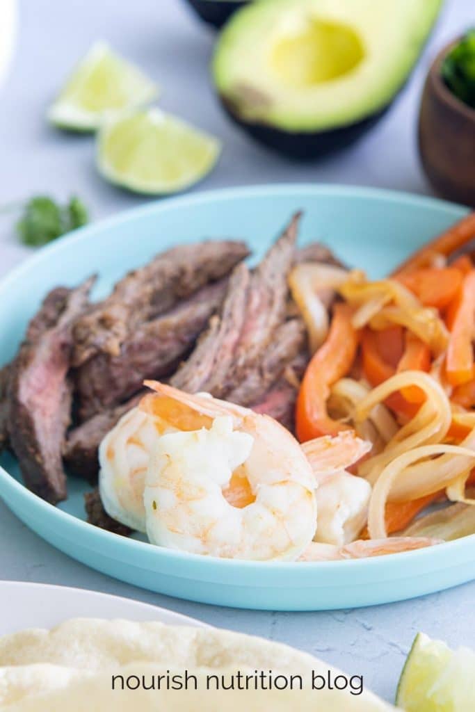 shrimp, steak, and vegetables in a blue bowl with other foods surrounding it