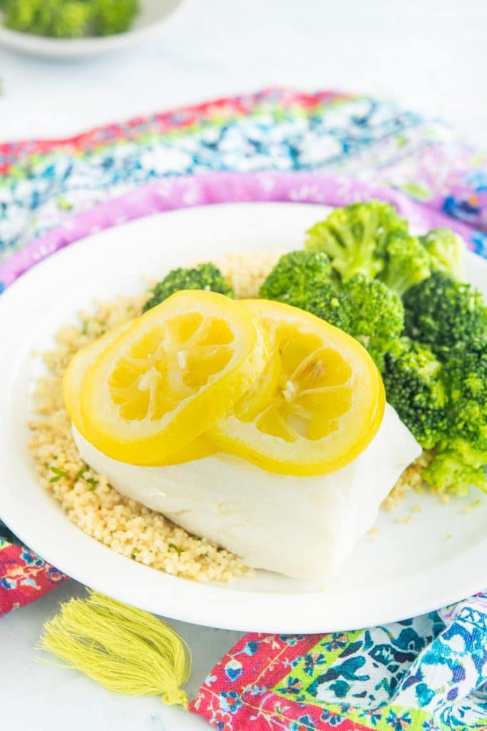 steamed cod with lemon slices on top next to broccoli