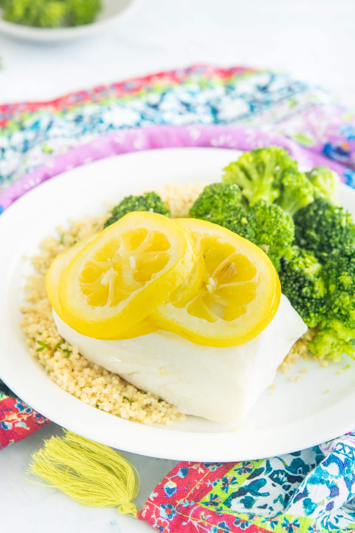 steamed cod with lemon slices on top next to broccoli