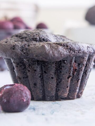 chocolate blueberry muffin standing on a table with blueberries surrounding it