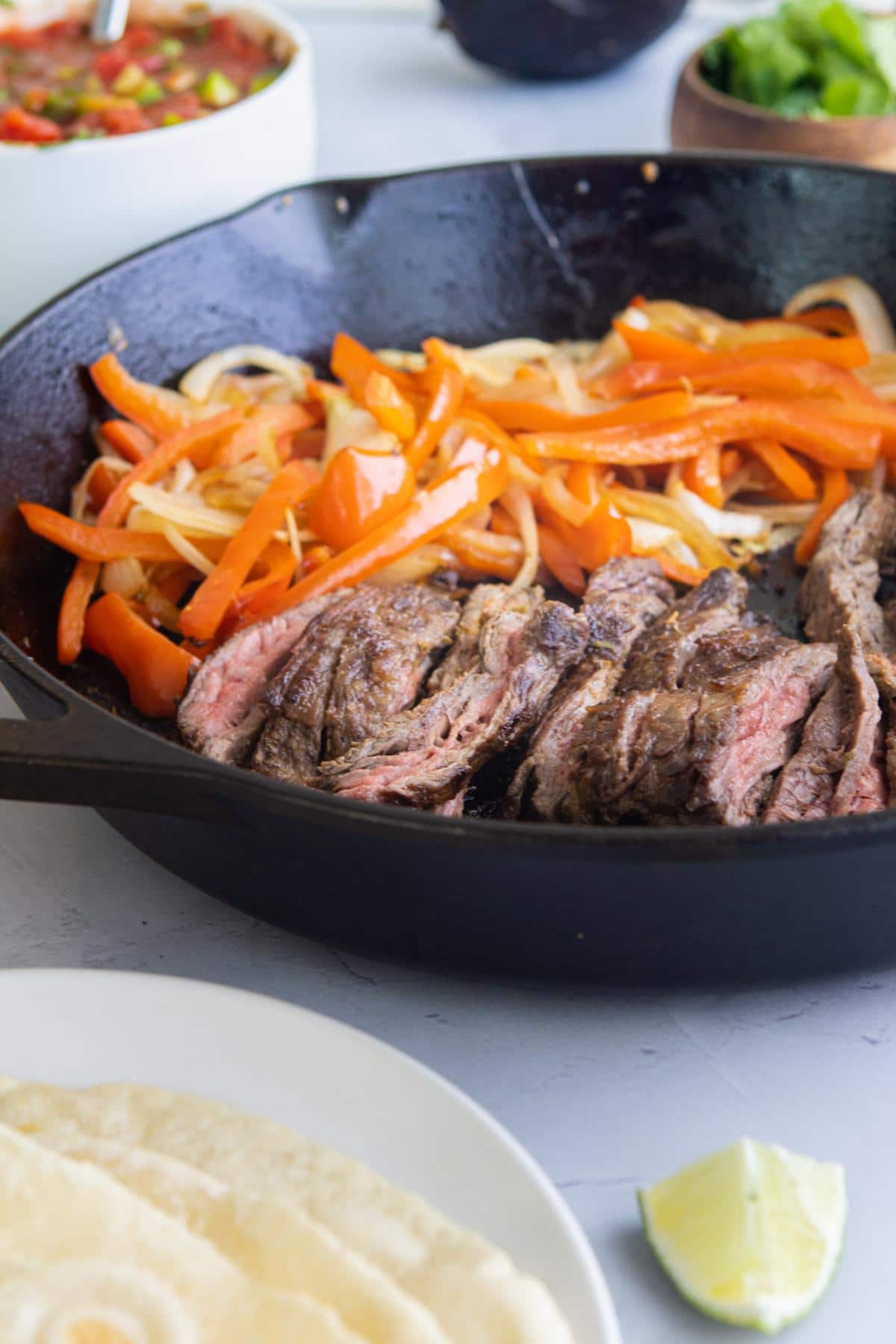 sliced steak, red bell peppers, and onions on a cast iron skillet