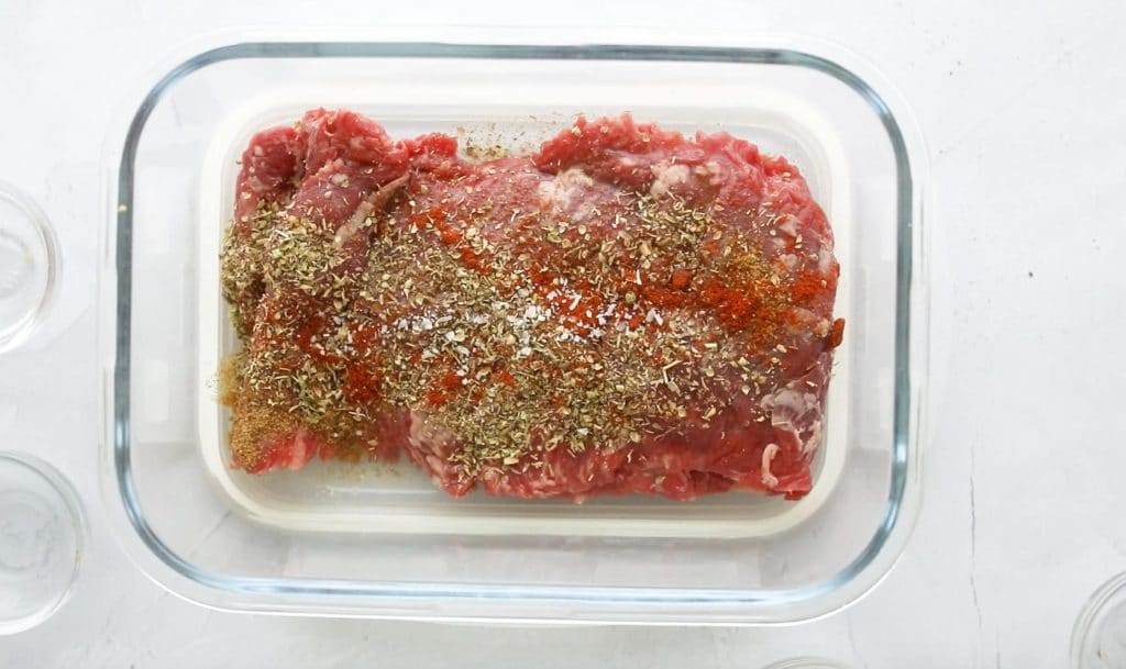 uncooked steak with spices in a glass container