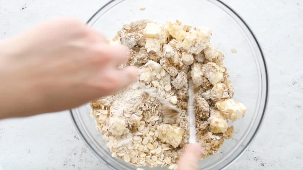 cutting butter into flour and oat mixture in a glass bowl