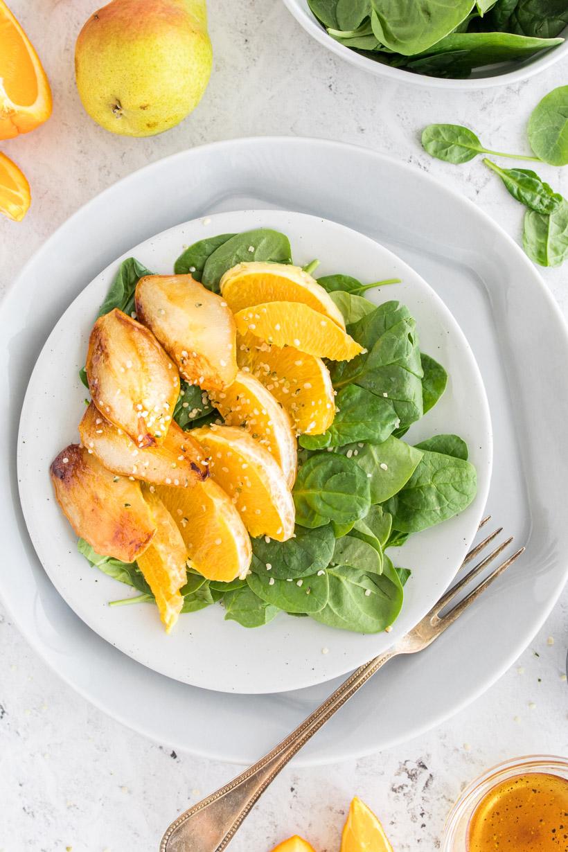 plate with spinach, orange slices, and roasted pears on it surrounded by ingredients