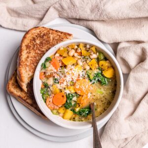 close up of delicata squash soup in a white bowl with grilled cheese
