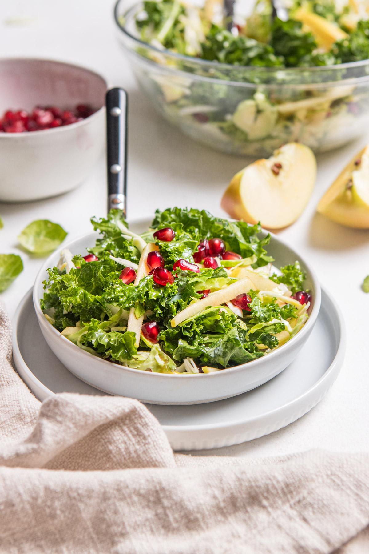 kale slaw with apples and pomegranates with ingredients surrounding it