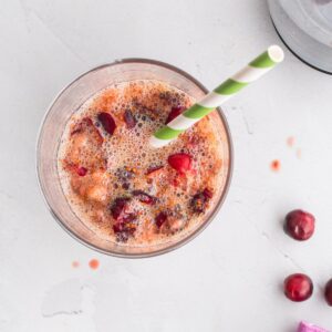 smashed cranberries and juice in a glass with a green striped straw