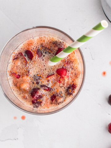 smashed cranberries and juice in a glass with a green striped straw