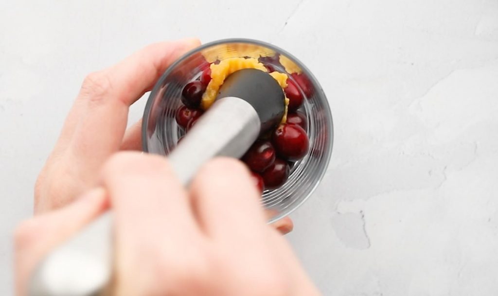 hand smashing cranberries and orange juice concentrate in a glass