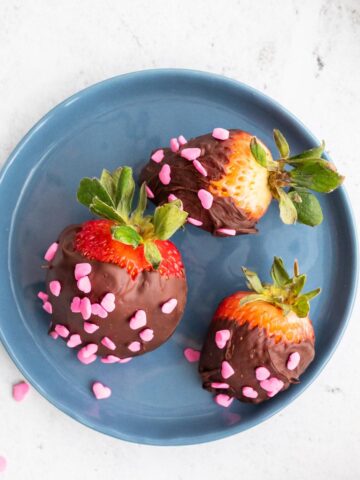 three chocolate covered strawberries on a blue plate