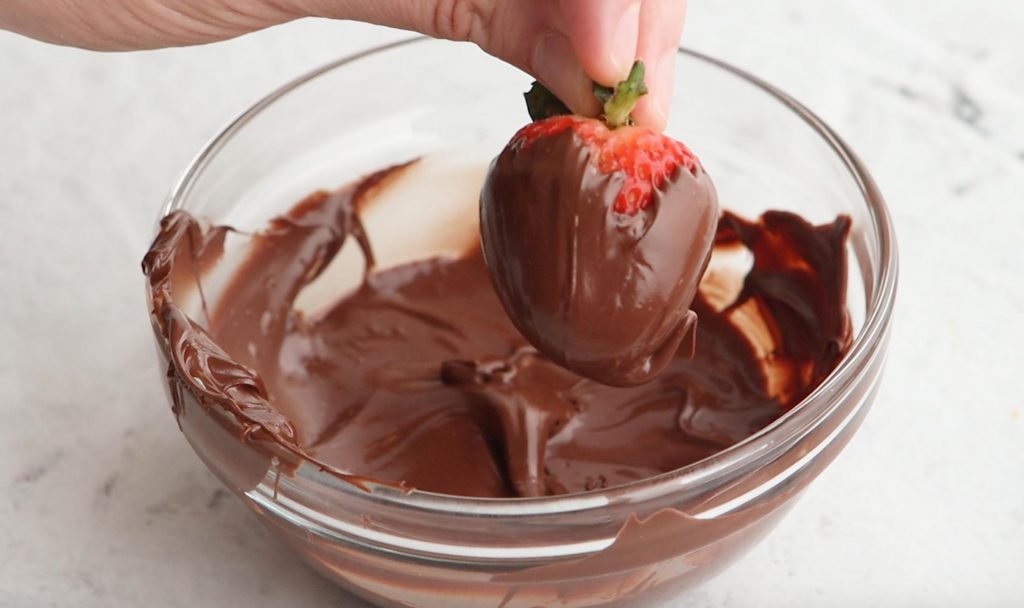 hand holding a small strawberry covered in chocolate