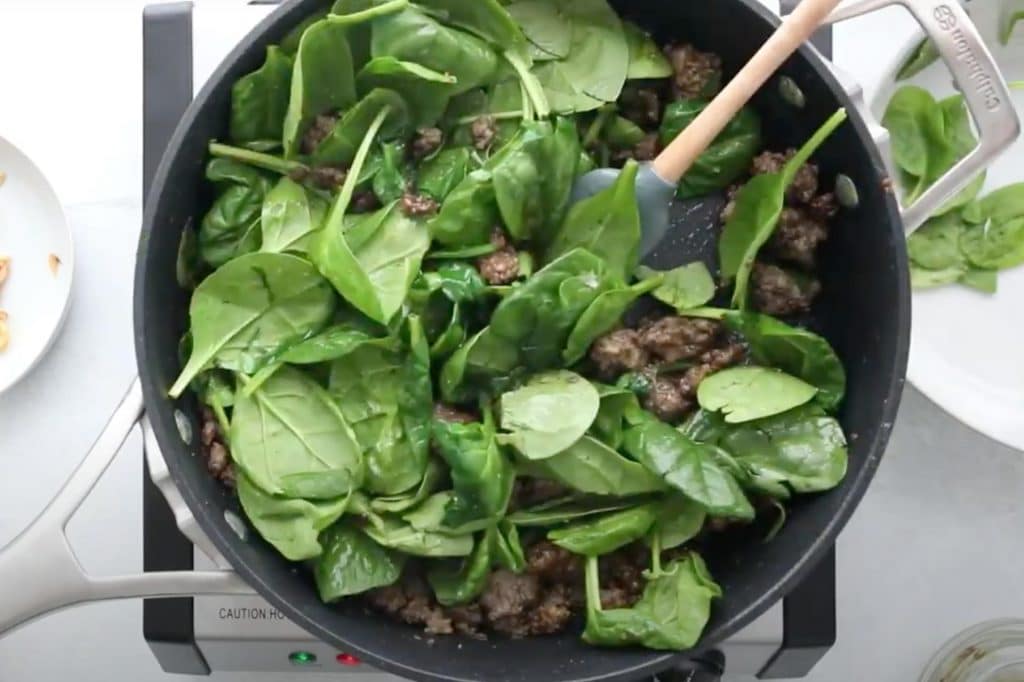 beef and spinach cooking in a black saucepan