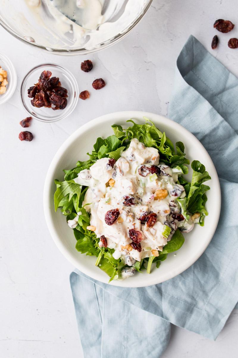 mixed greens with chicken salad on top in a white bowl with ingredients around it