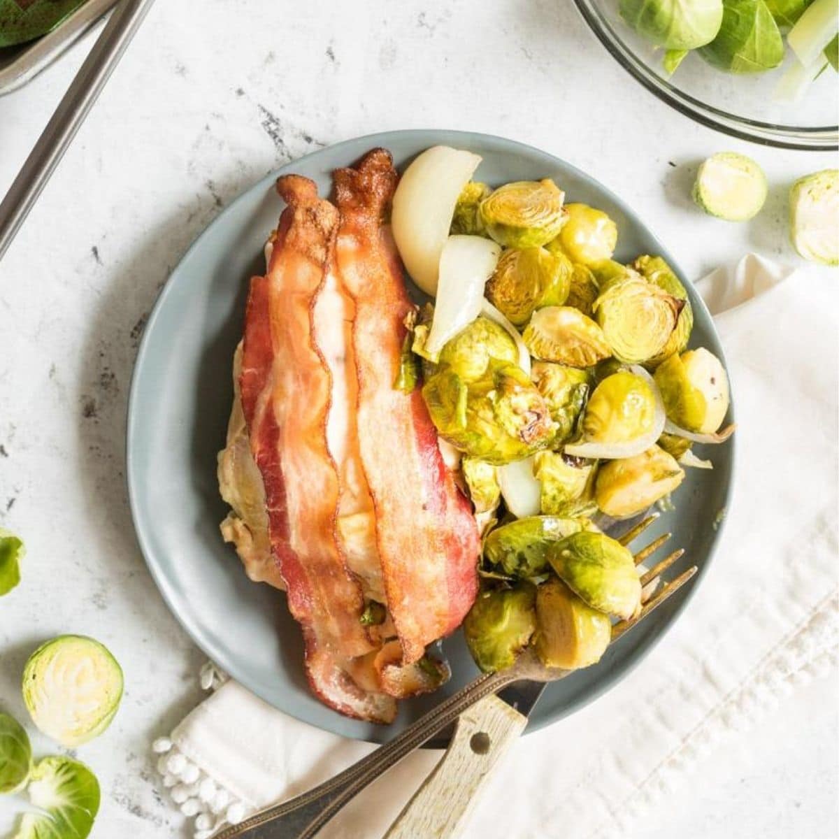 chicken with bacon on top next to brussels sprouts on a grey plate