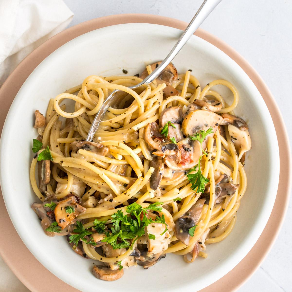 close up of pasta with mushrooms, bacon, and chicken with a fork in it