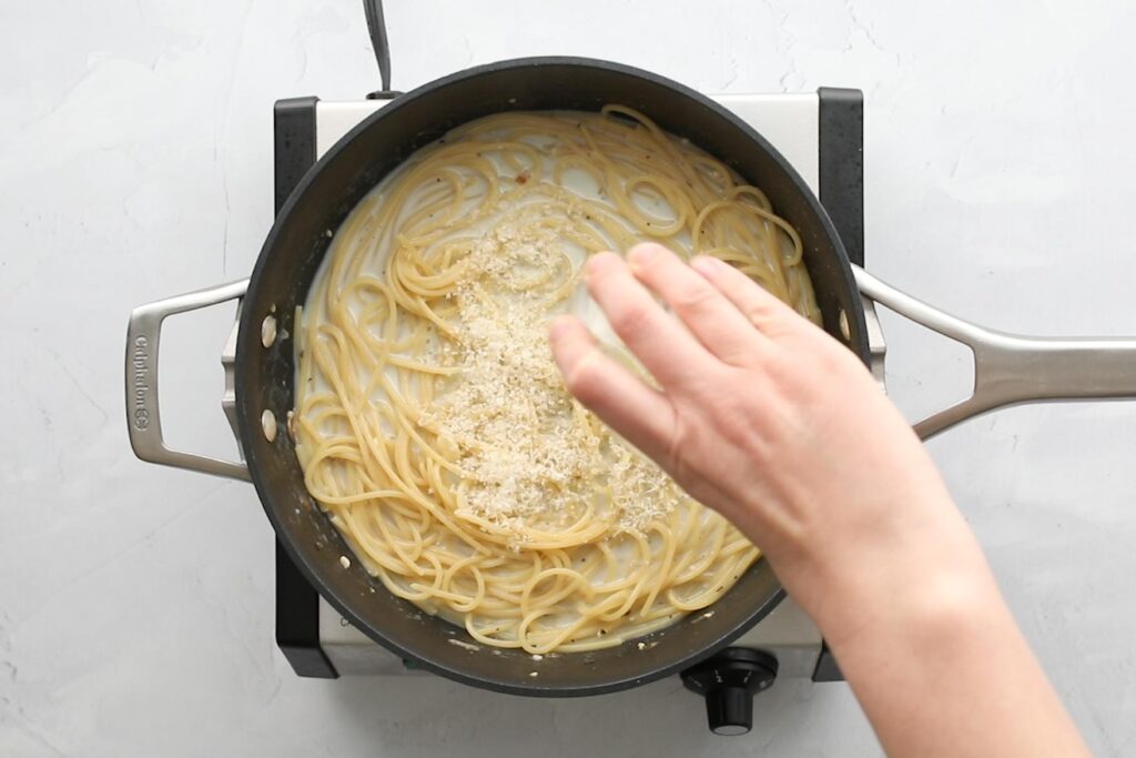 sprinkling parmesan cheese over pasta in a frying pan