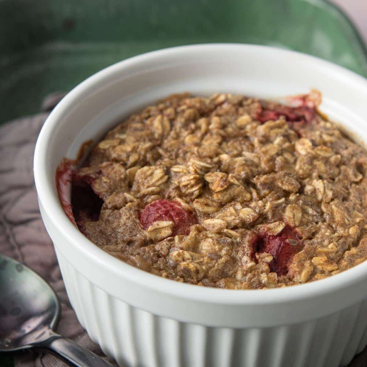 one baked oatmeal cup on a white plate with more cups around plate