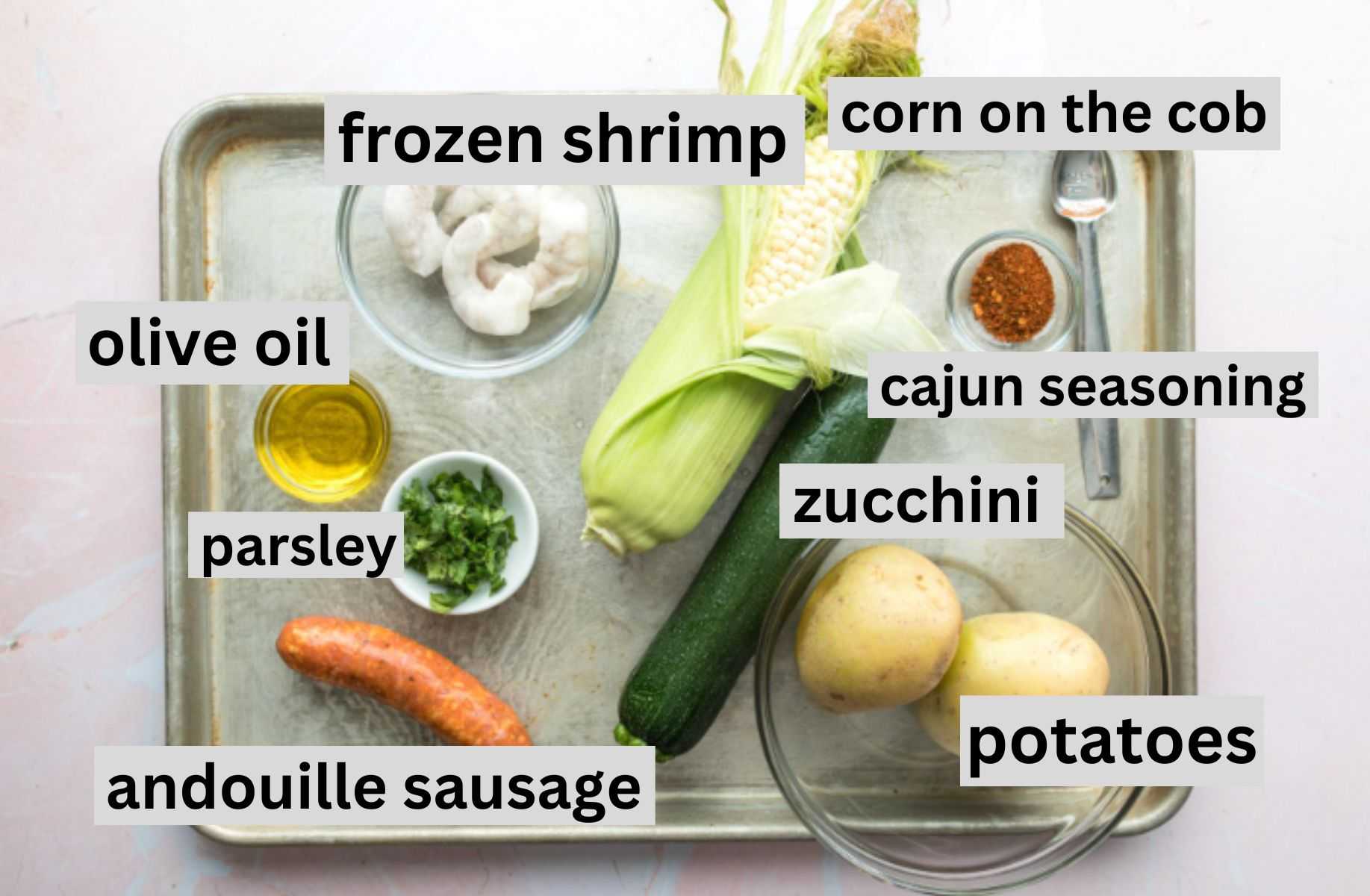 corn, zucchini, potato, sausage, shrimp, and spices on a baking sheet