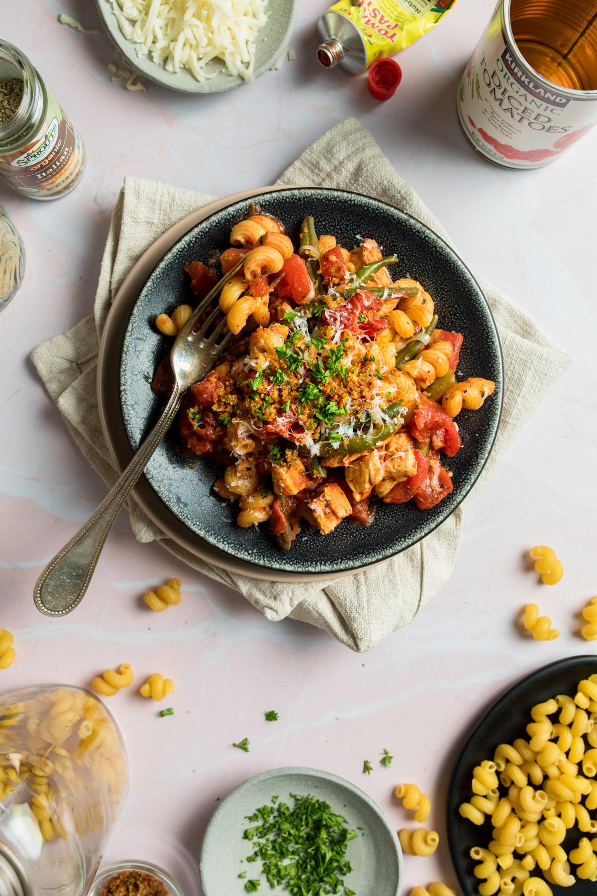 spiral pasta with tomatoes on a black plate with ingredients around it