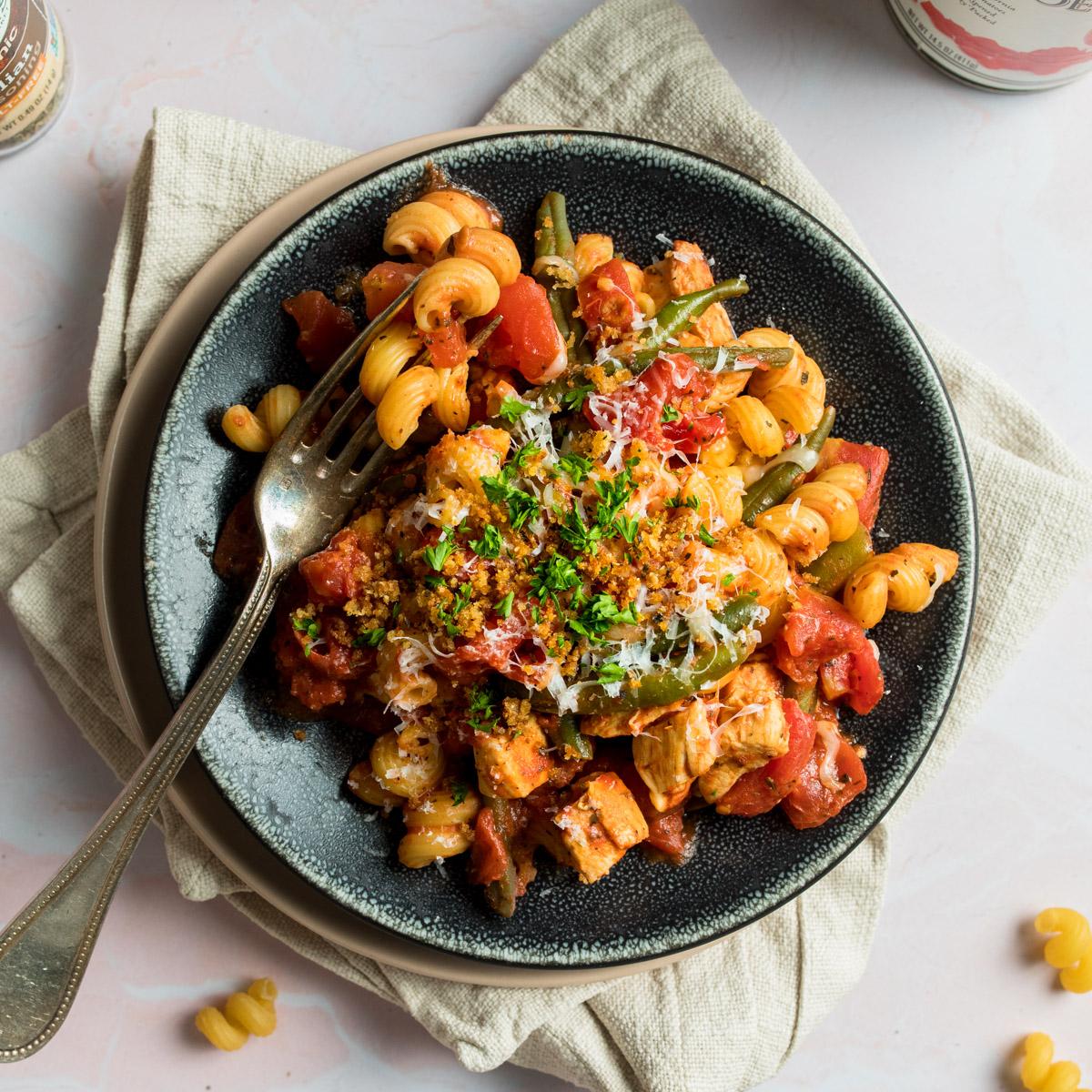 square photo of spiral pasta with tomatoes on a black plate with a fork