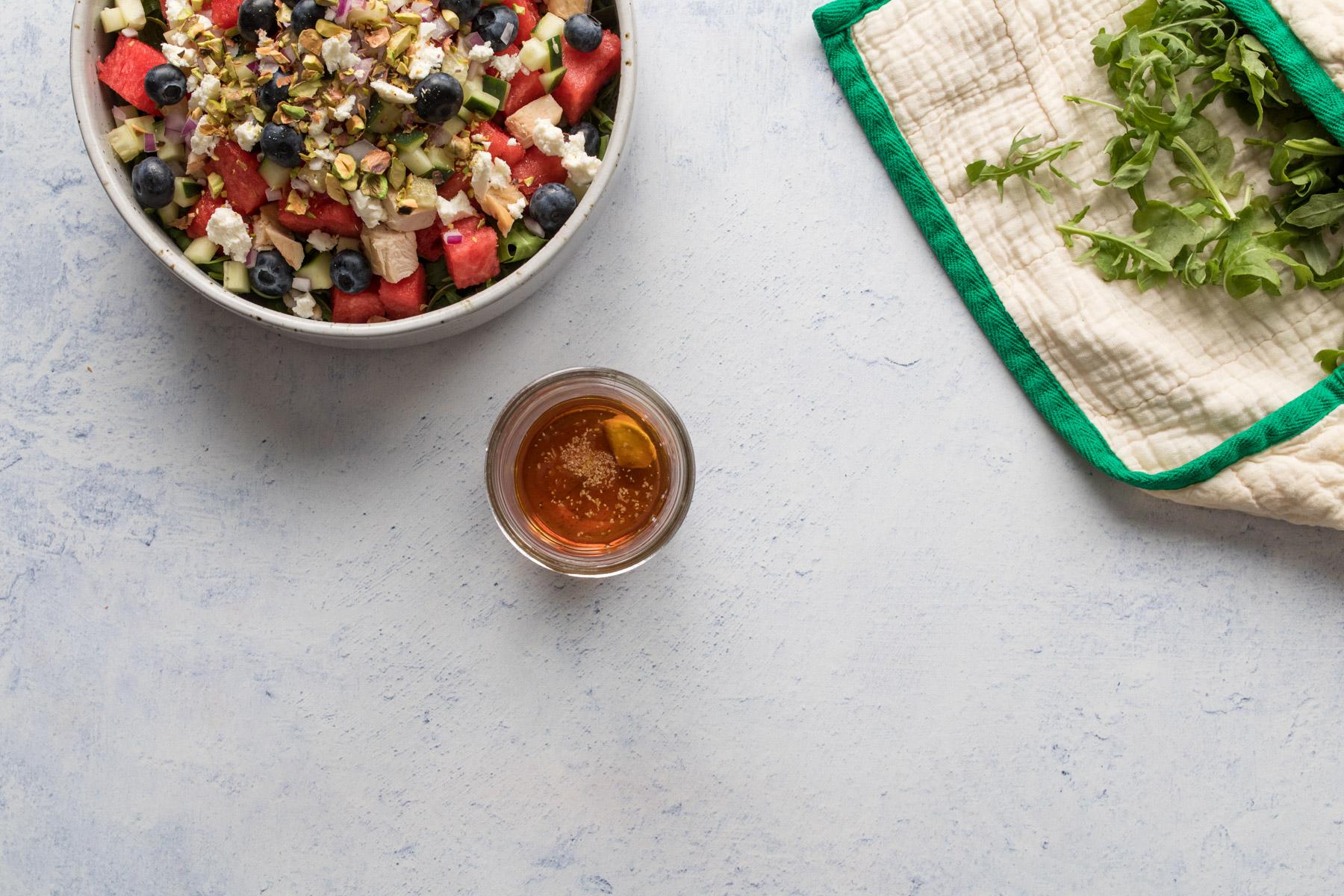 jar of salad dressing on a table next to a salad and arugula