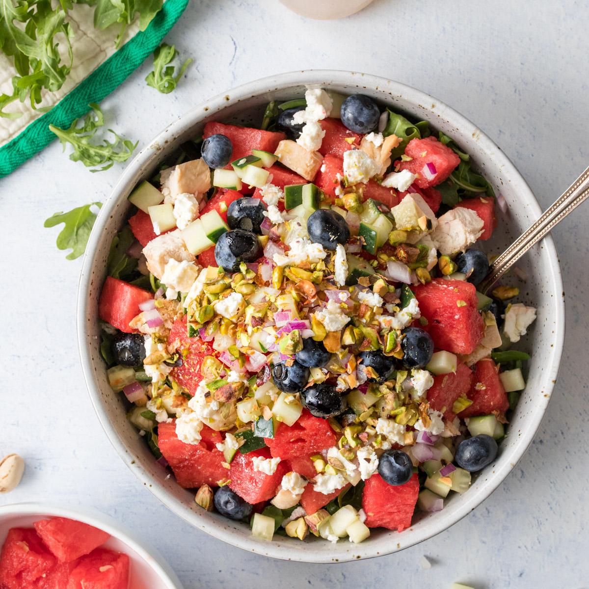 large bowl full of watermelon, blueberries, feta cheese on a table