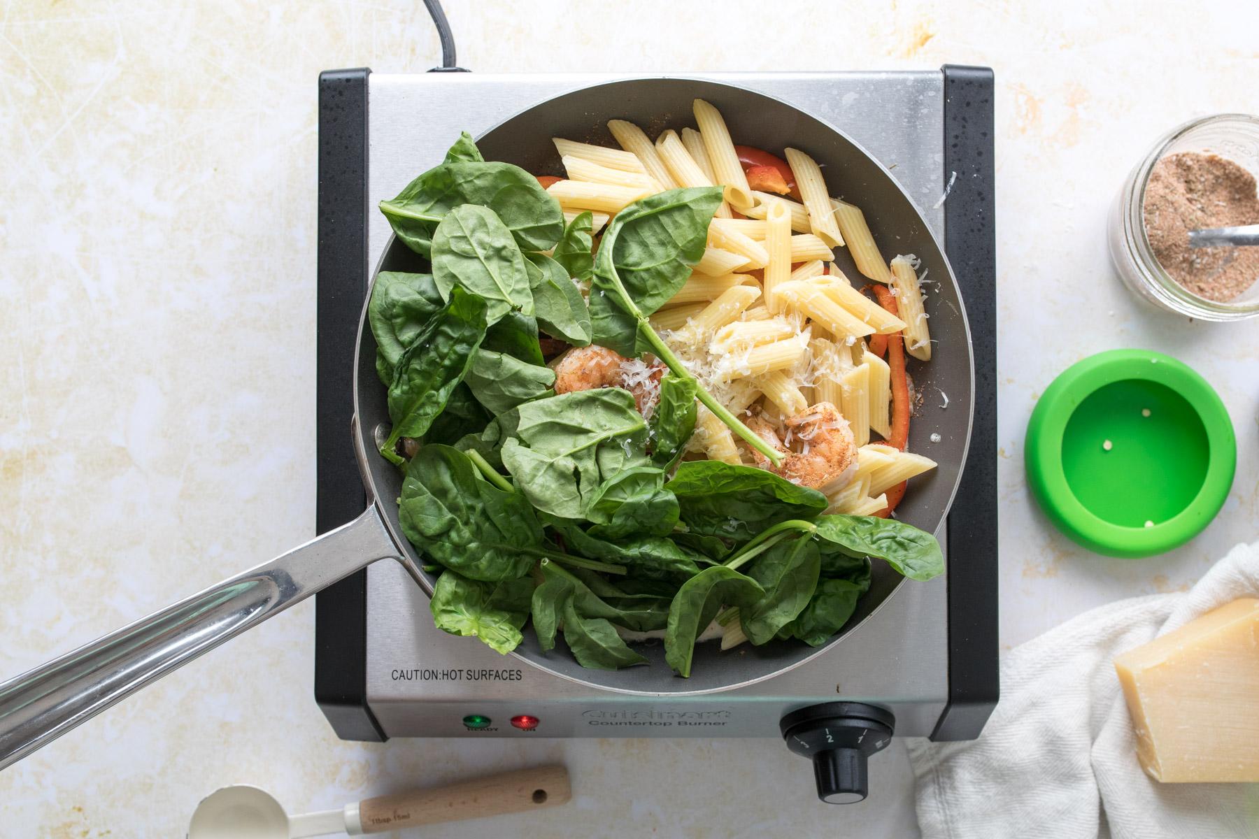 spinach, pasta, shrimp, and bell peppers in a skillet