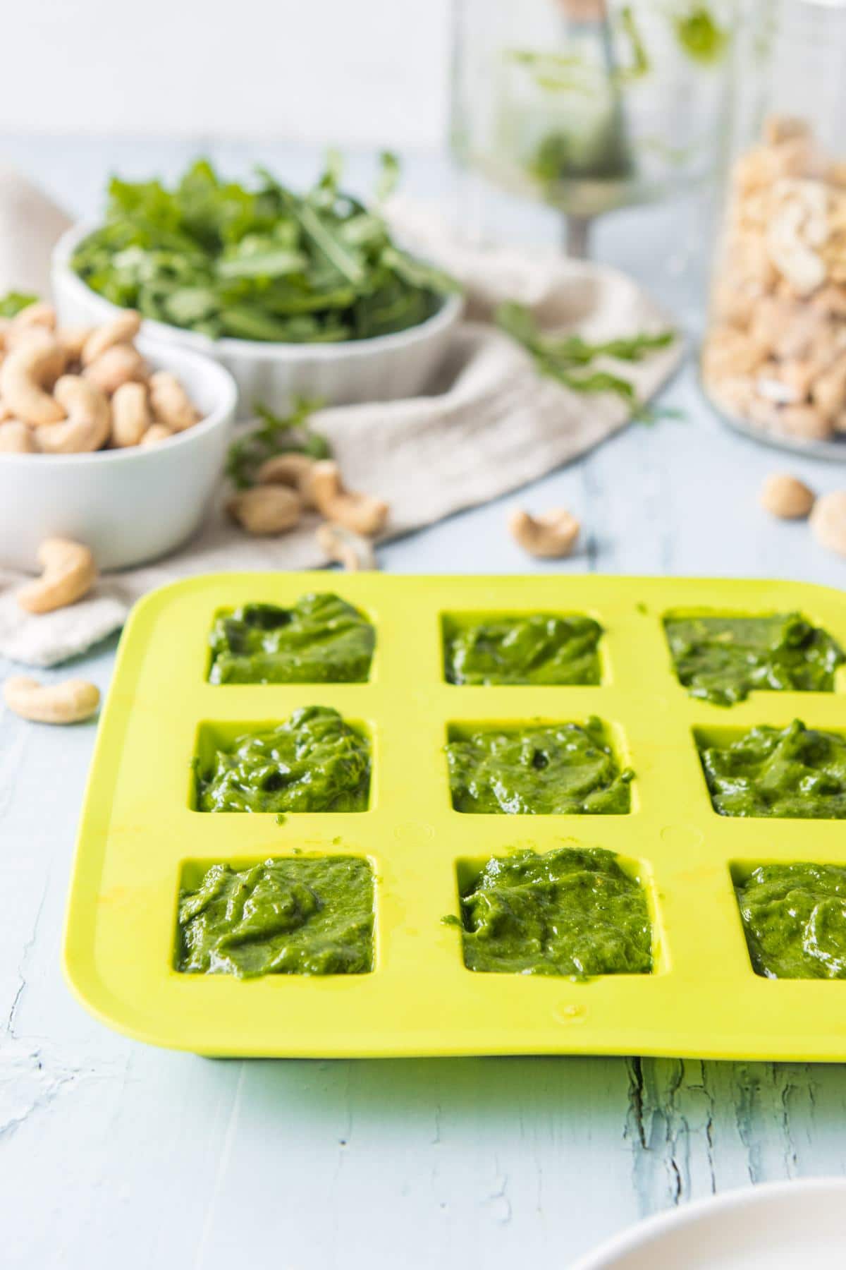 Green ice tray full of pesto on a table