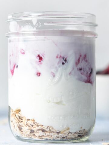 close up of a glass jar full or oats, yogurt, berries, and milk