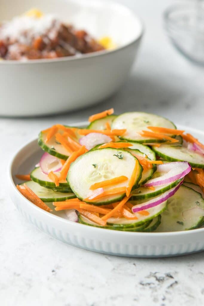 carrot cucumber salad on a plate with pasta in background