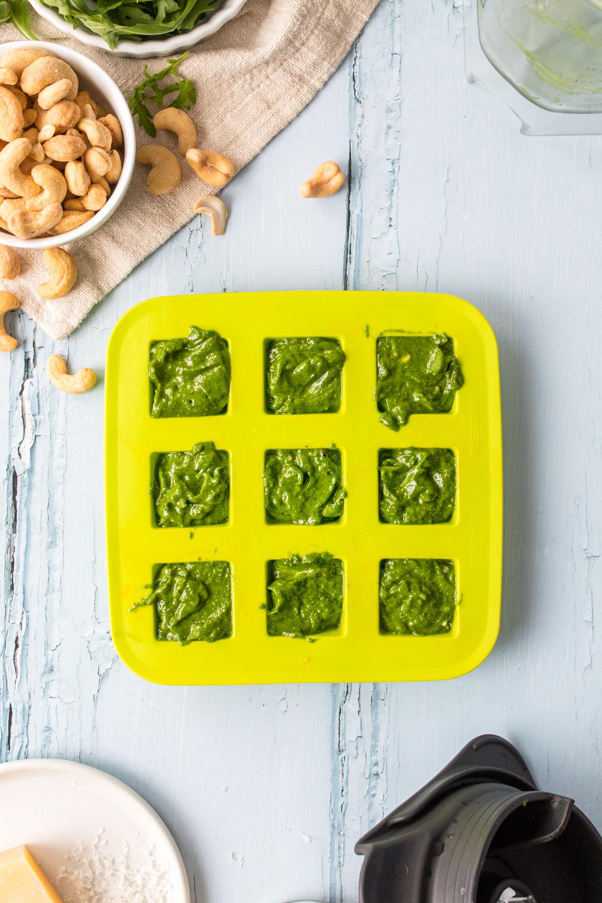 pesto in a green ice tray with ingredients around it