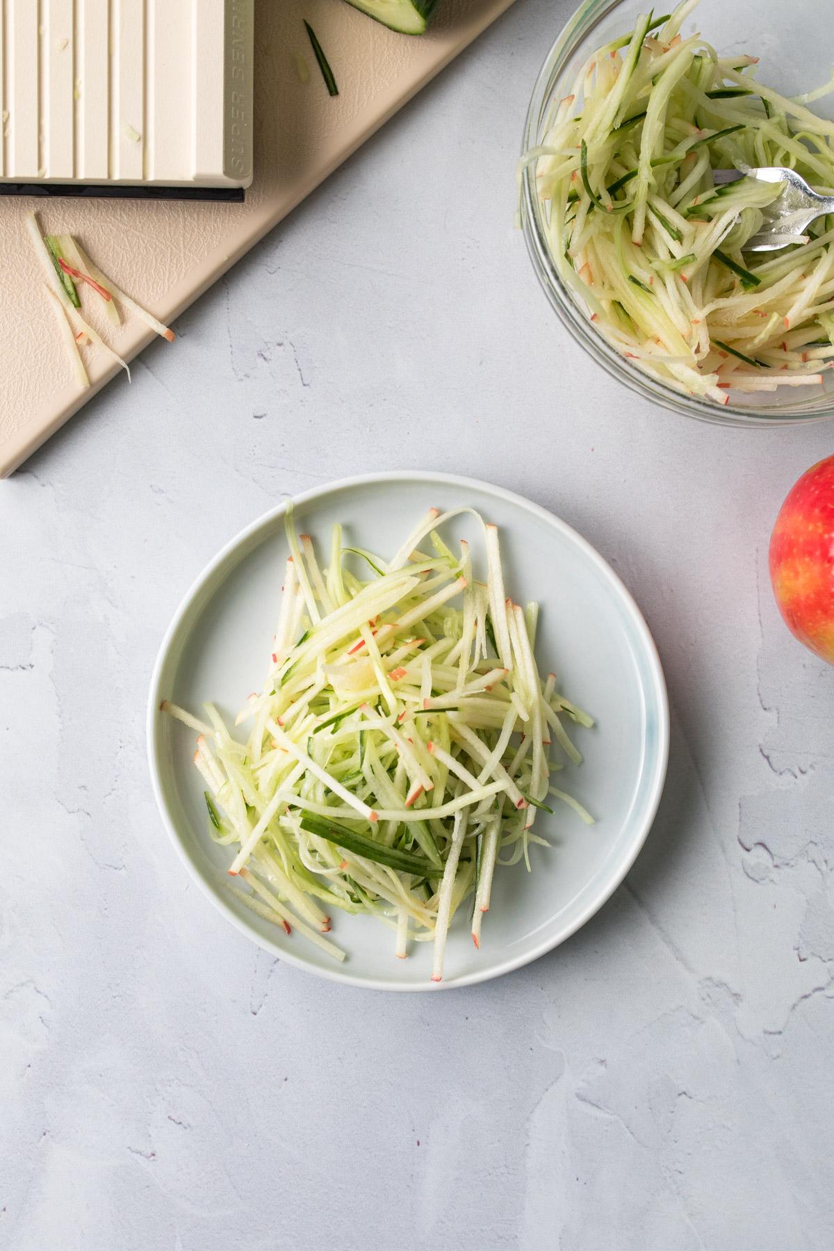 julienned apples and cucumbers on a plate with ingredients around it