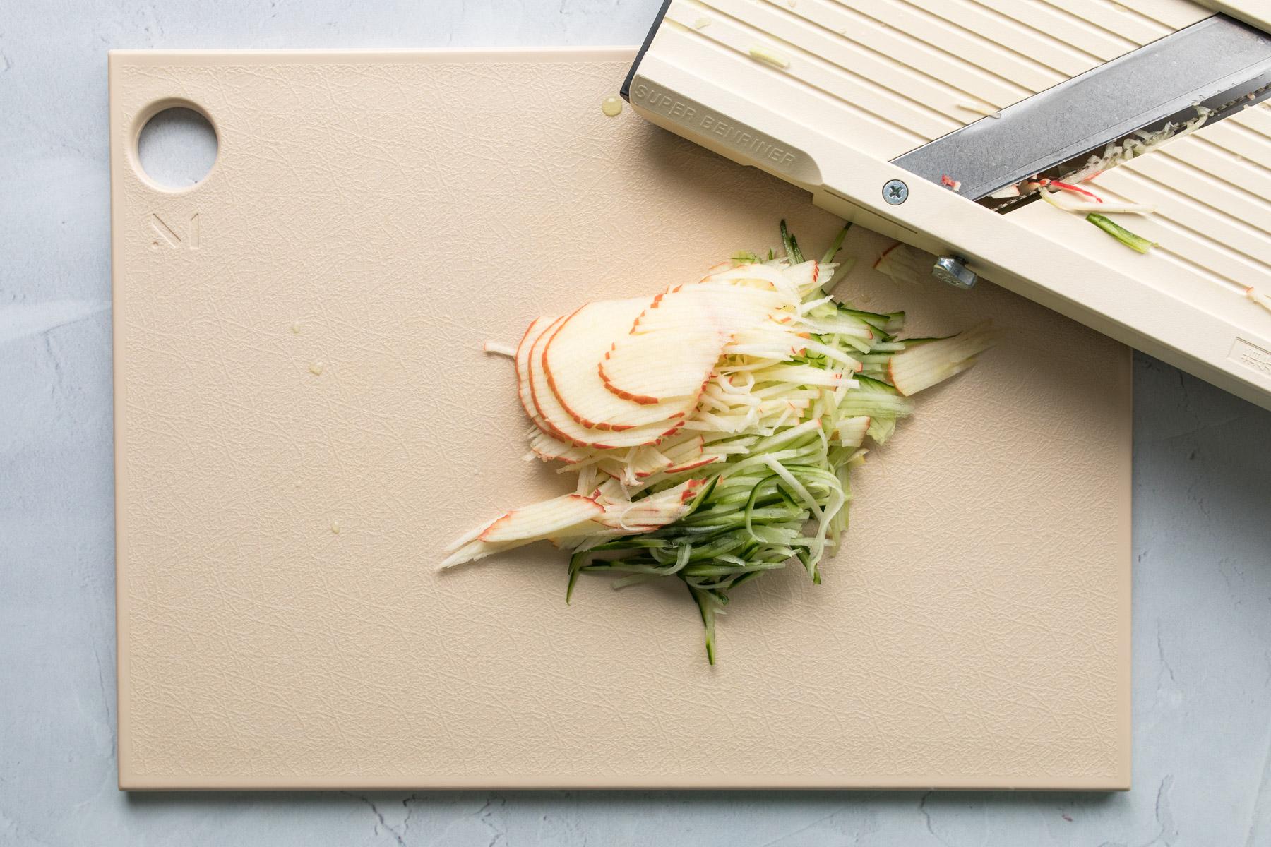 thinly sliced apples and cucumbers on a cutting board