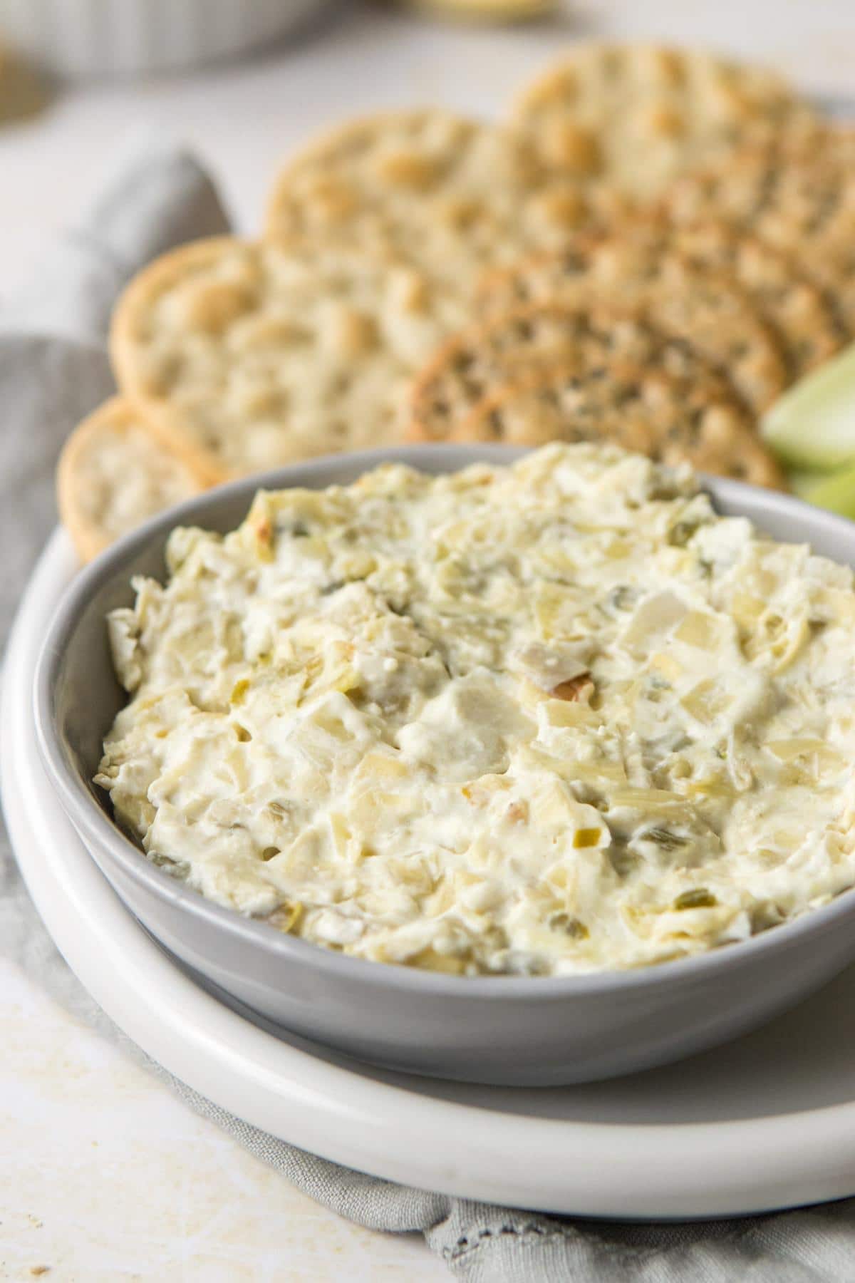 artichoke dip in a bowl with crackers behind