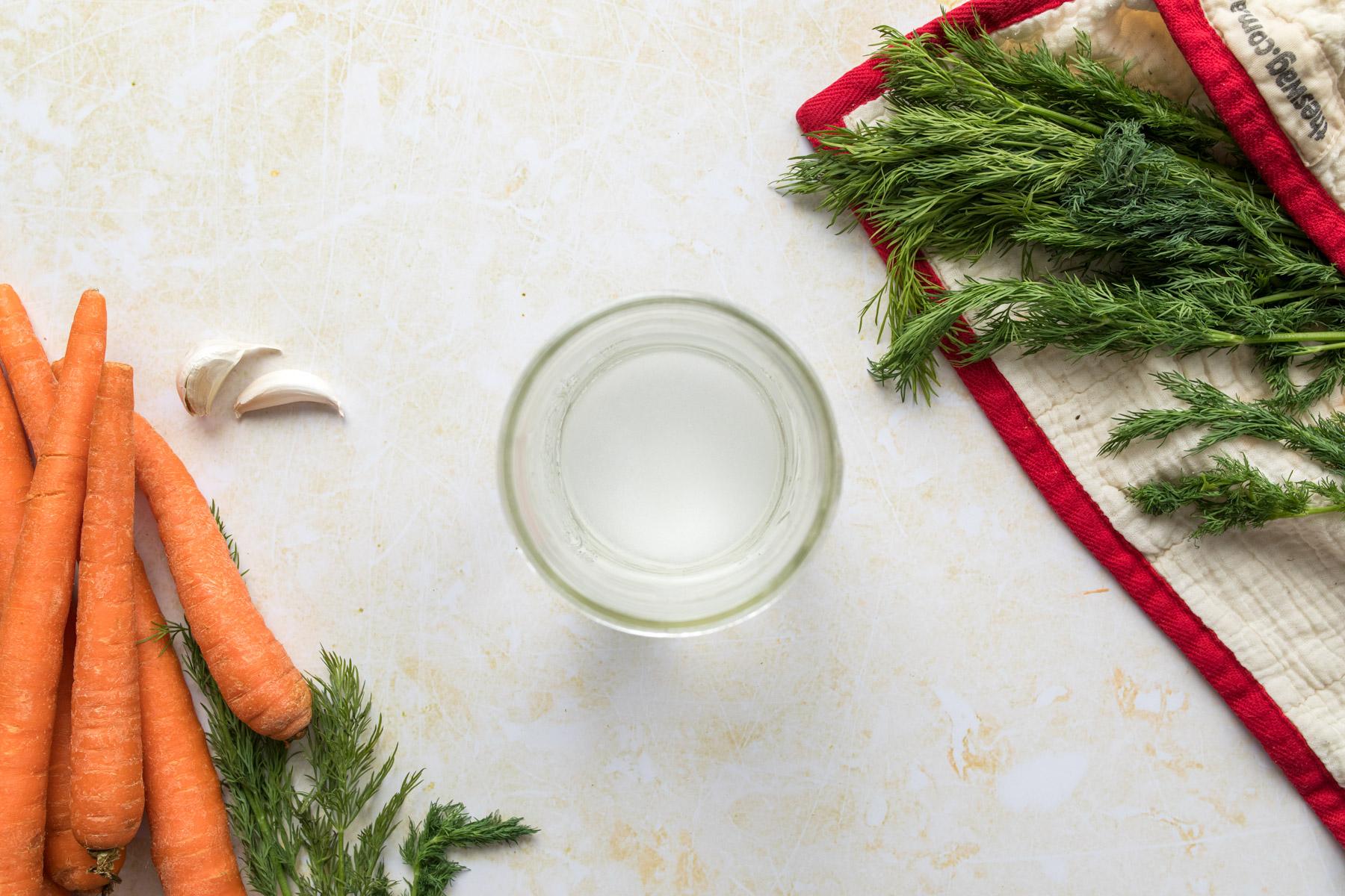 jar of water surrounded by dill and carrots