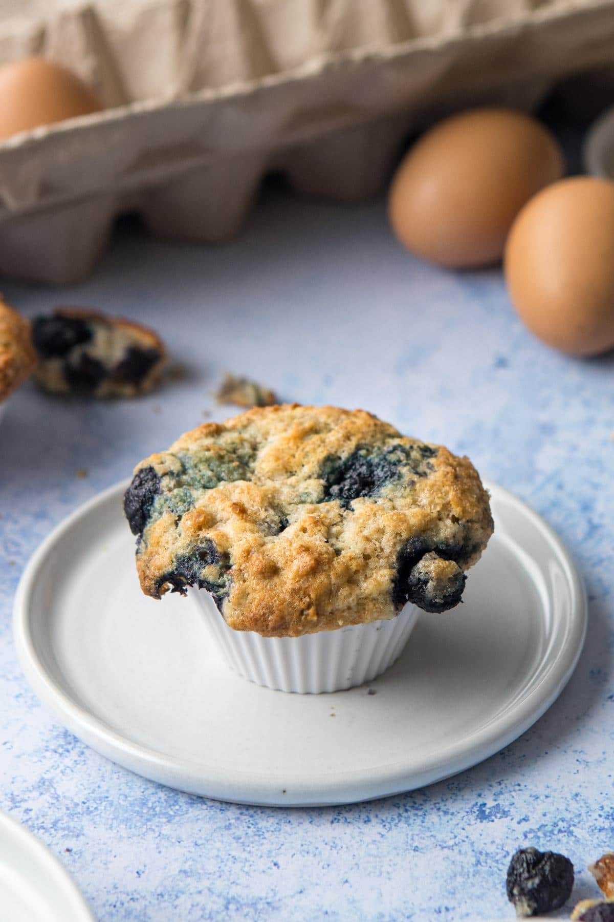 blueberry muffin on plate with eggs behind