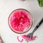 square image of pink pickled onions with fork