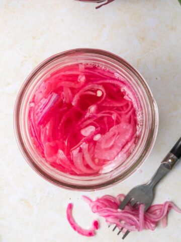 square image of pink pickled onions with fork