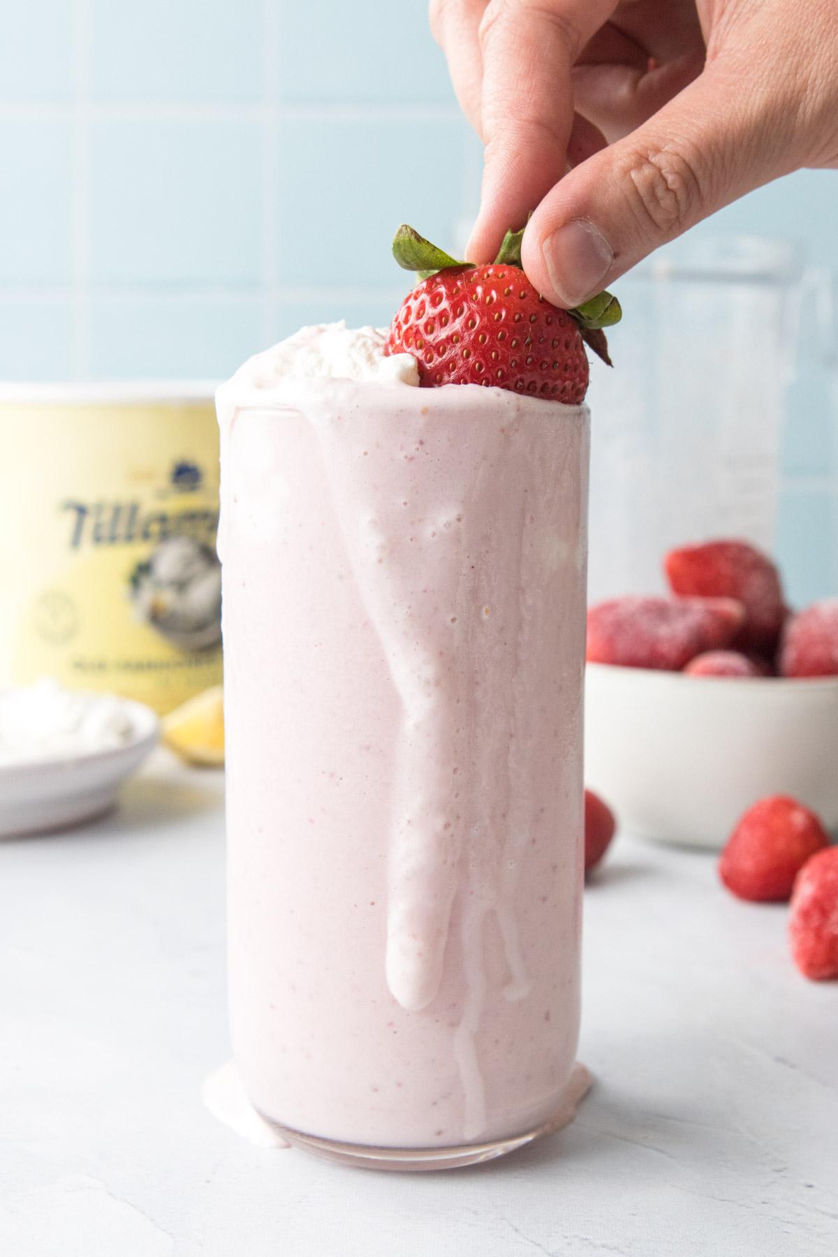 hand pushing strawberry into milkshake in glass
