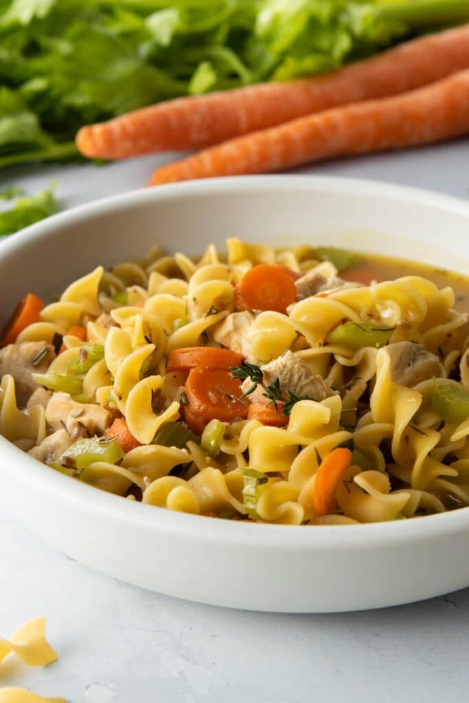white bowl of egg noodles, vegetables in soup