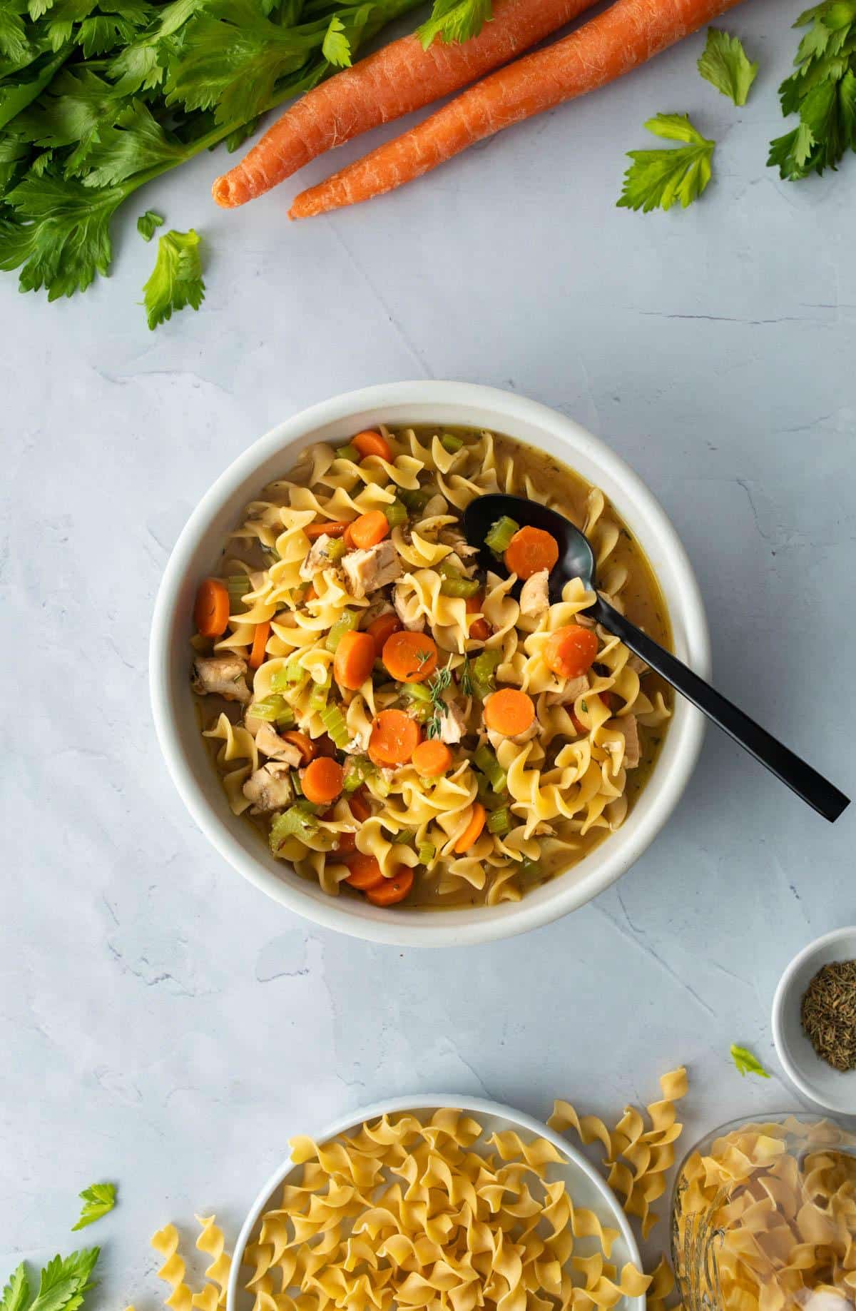 white bowl of chicken noodle soup with black spoon