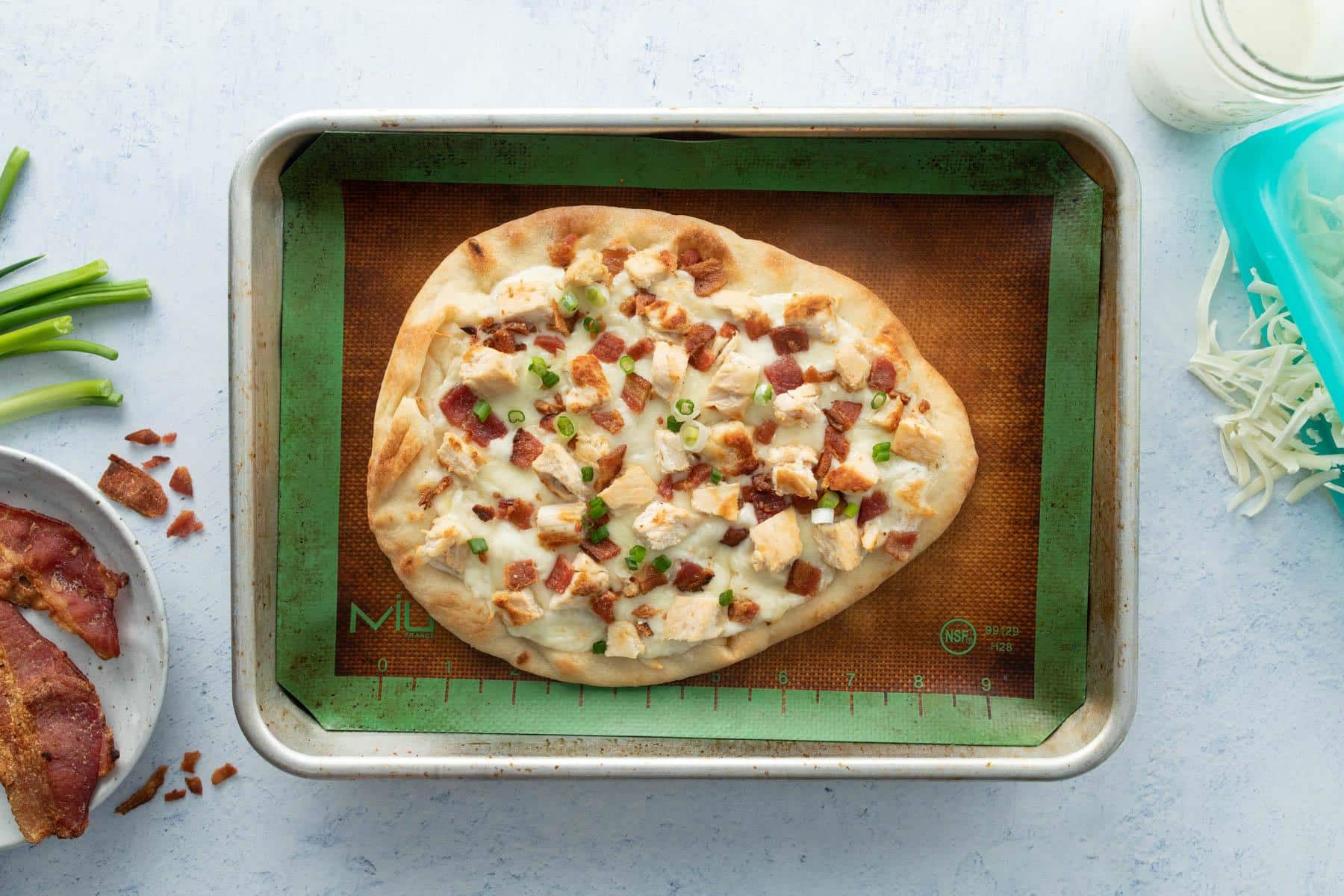 cooked pizza with bacon, chicken, and green onions on it