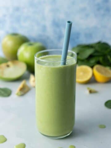 green smoothie in glass with blue straw, ingredients behind