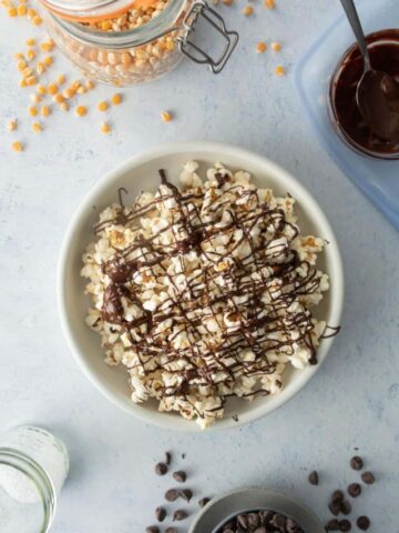 bowl of popcorn with chocolate drizzle with ingredients around it