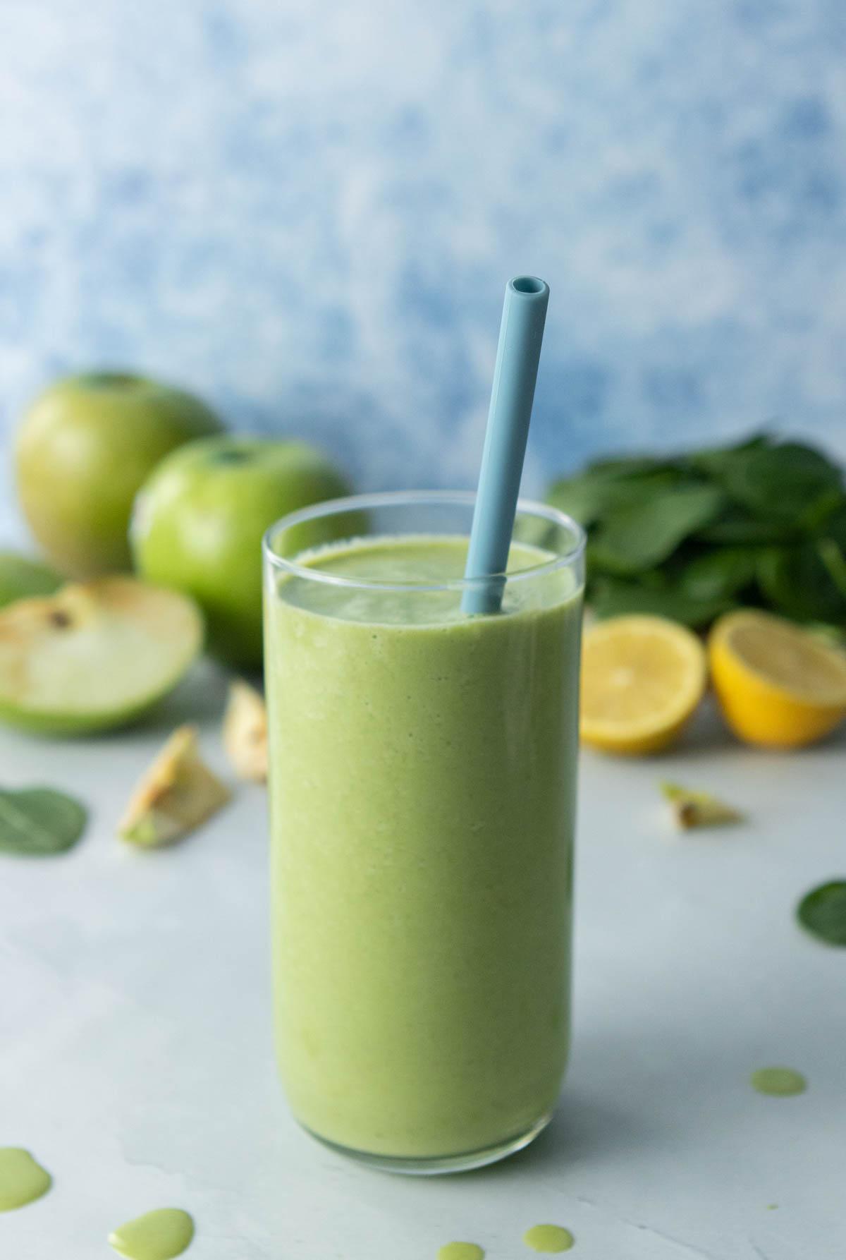 green smoothie in glass with blue straw, ingredients behind