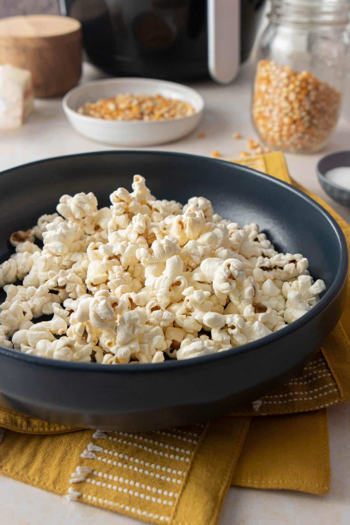 dark blue bowl full of popcorn with popcorn kernels in back