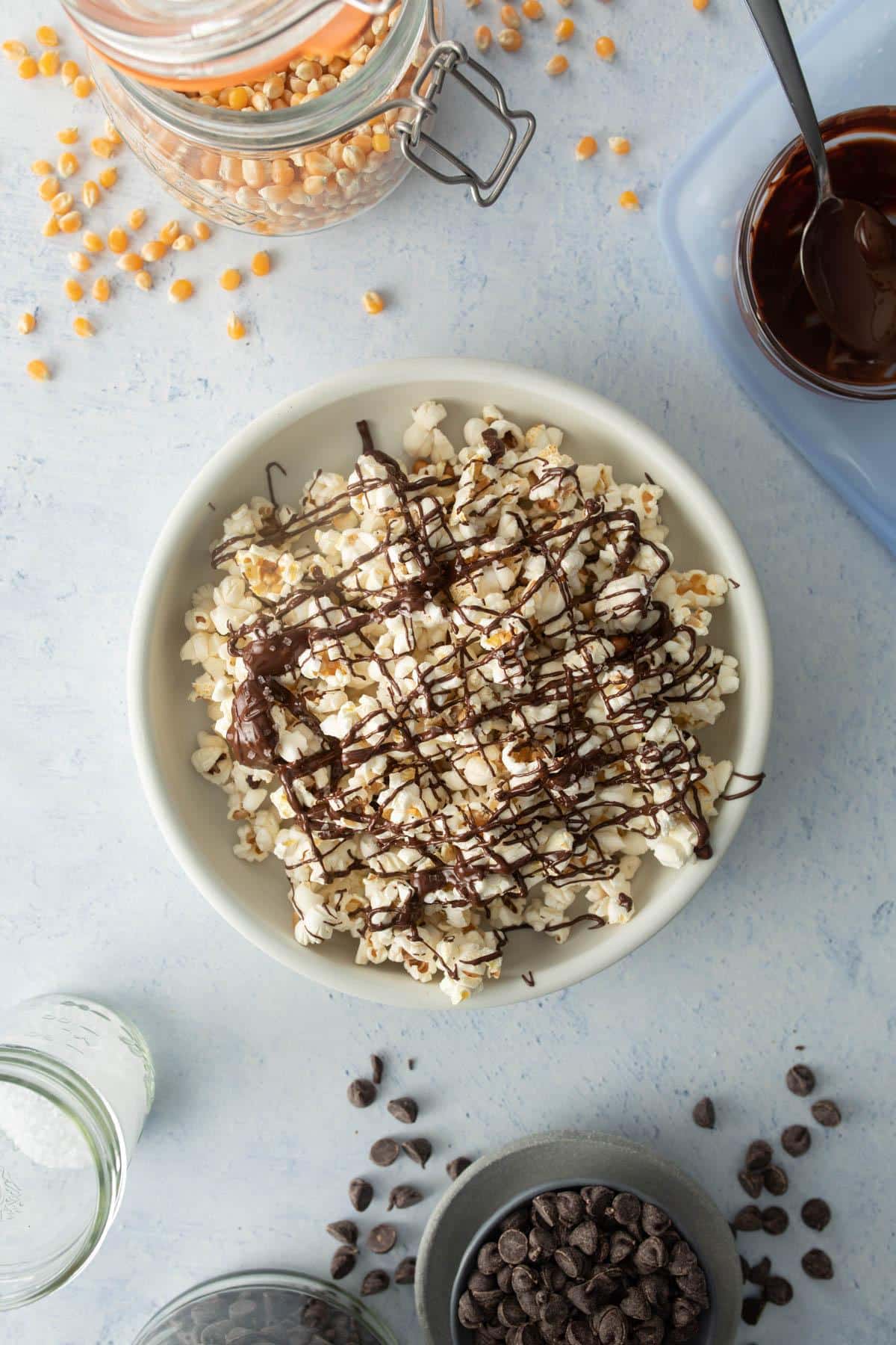 bowl of popcorn with chocolate drizzle with ingredients around it