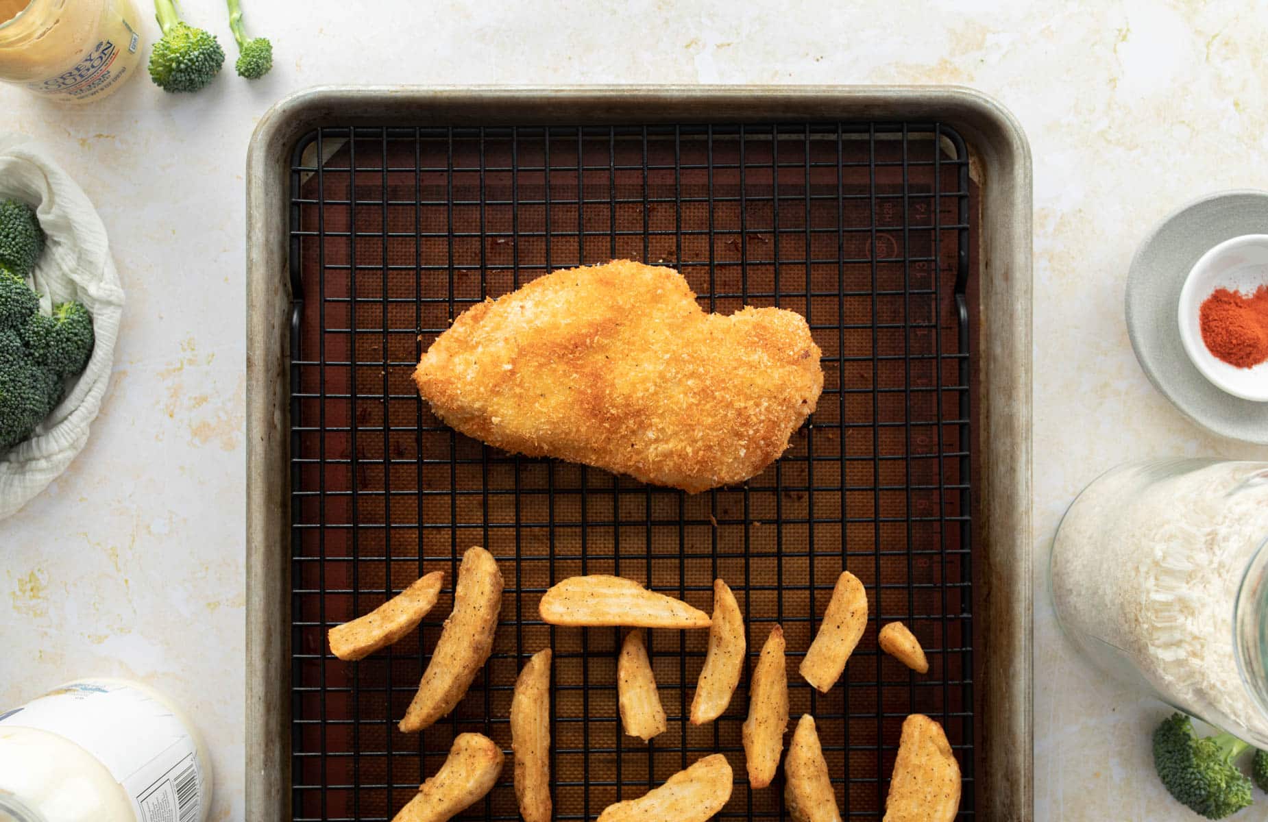 baked breaded chicken, potato wedges on baking sheet