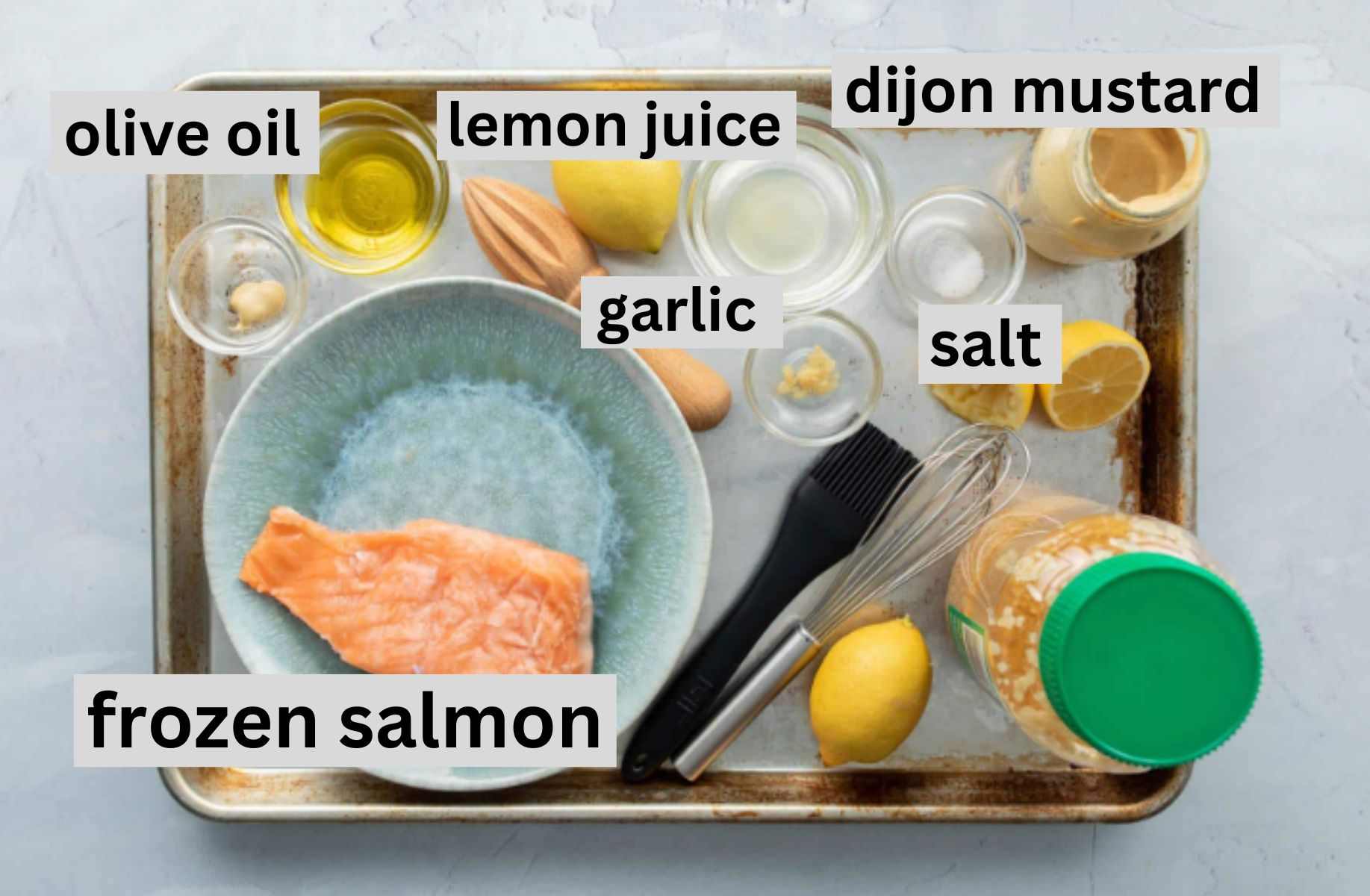 baking sheet with salmon filet on plate, lemons, and other ingredients on it