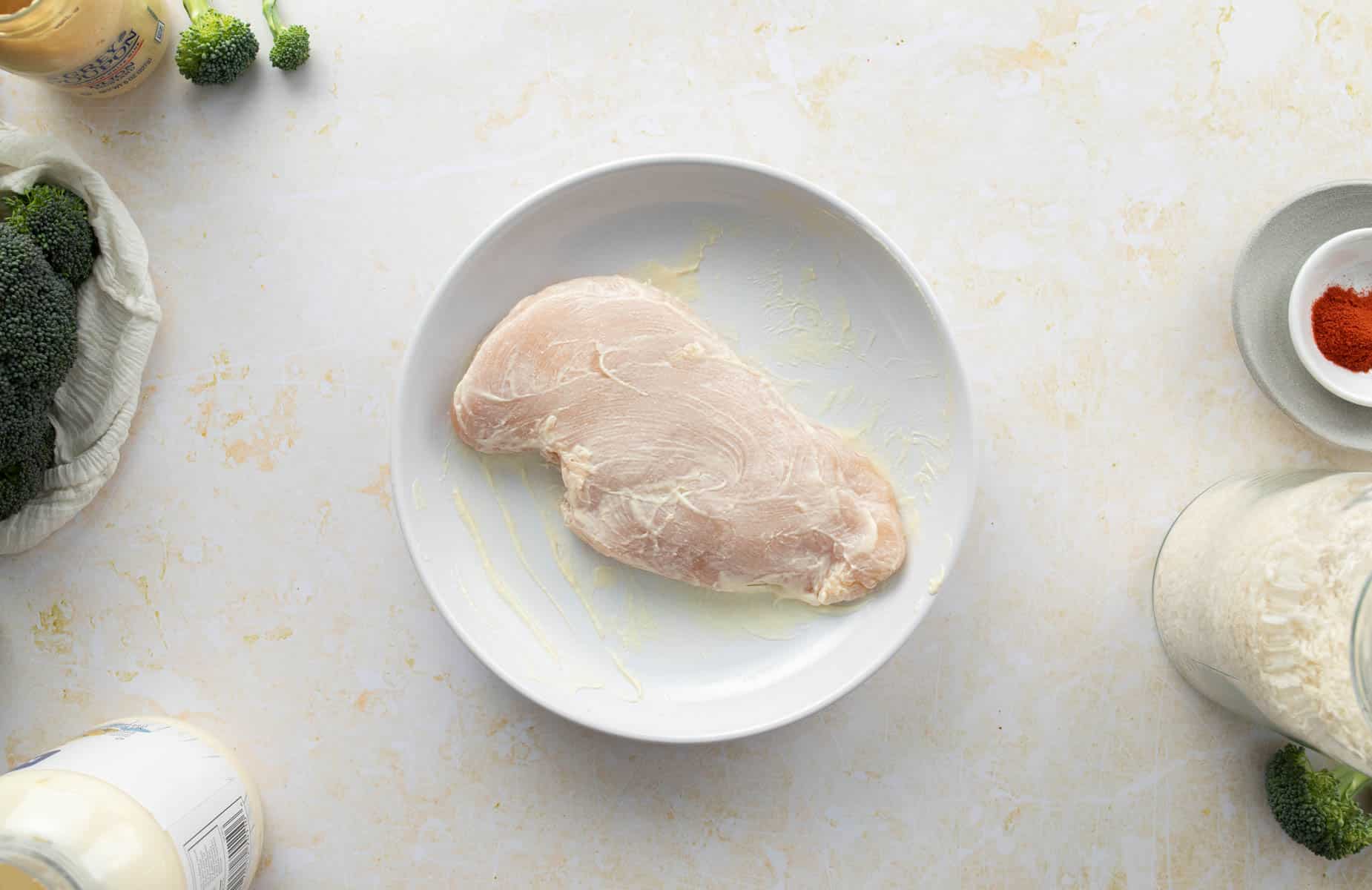 chicken breast covered in mayonnaise in shallow plate